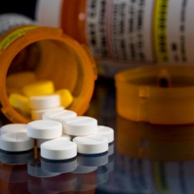 a close up of a tipped over orange container with white pills spilling onto a black surface